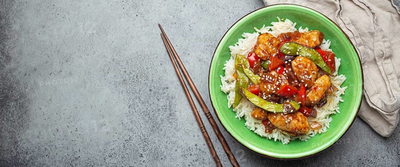 Asian sweet and sour sticky chicken with vegetables stir-fry and rice in ceramic bowl with chopsticks top view on gray rustic stone background, traditional Asian dish. Space for text, food photography, food photography