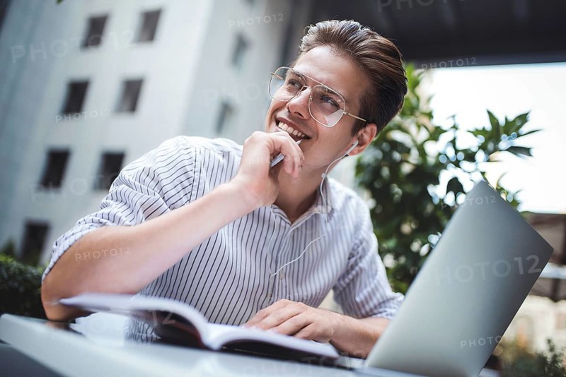 Happy handsome businessman mixes his break and job outdoors, businessman with headphones write some new ideas in notebook sitting in cafe