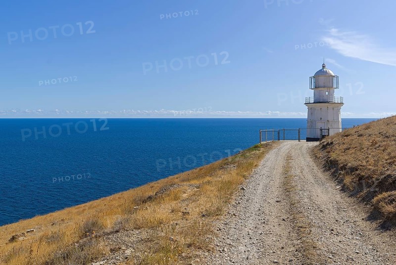 A dirt road running along a deserted mountainside to a lighthouse on the seashore. Cape Meganom, Crimea, a sunny day in September