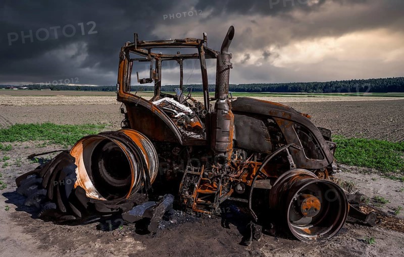 Fully destroyed burnt down tractor on a field