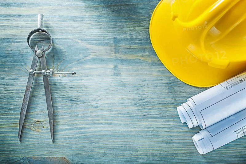 Pair of compasses blueprints hard hat on wooden board construction concept