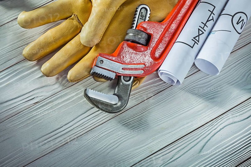 New plumb wrench leather gloves and rolled piping blueprints on vintage wood background