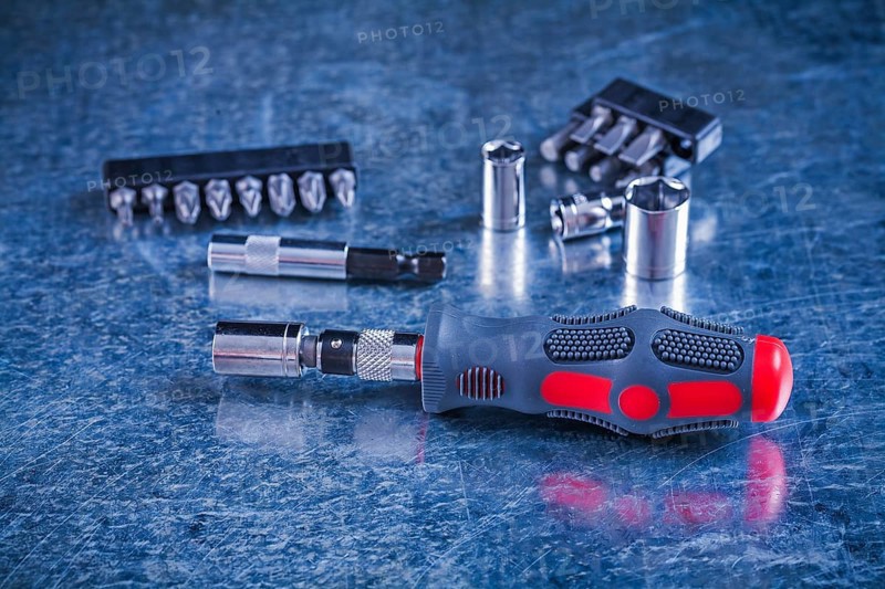 Insulated screwdriver with interchangeable bits and heads on scratched metallic background construction concept