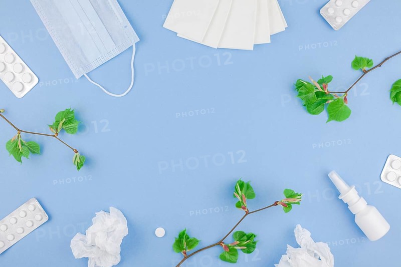 Creative flat lay concept of seasonal spring pollen allergy with napkins, pills, face mask, drops in a bottle and fresh green sprouts with buds with copy space background minimal style, template for text