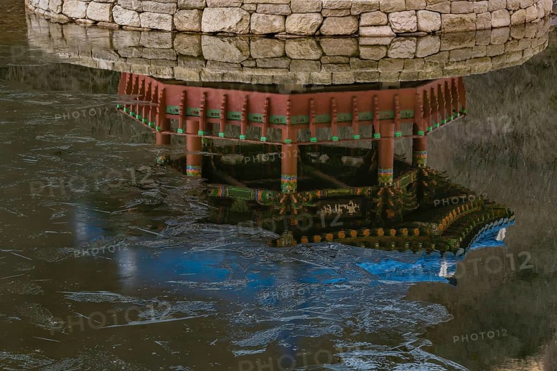 Jeongeup-si, South Korea. December 8, 2020: Reflection in water of picnic pavilion with blue roof on stone island in middle of pond