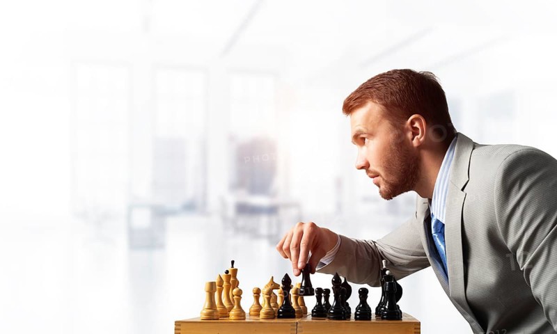 Businessman moving chess figure in chessboard. Successful management and leadership concept. Handsome man in business suit sitting at desk with chess. Operative tactics and strategy planning