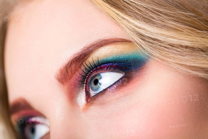Close up portrait of a beautiful young blond model with bright make up. Close up of abstract multicolor make up. Makeup Pigment powder explosion