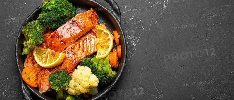 Healthy baked fish salmon steaks, broccoli, cauliflower, carrot in cast iron casserole bowl black dark stone background. Cooking a delicious low carb dinner, healthy nutrition, food photography