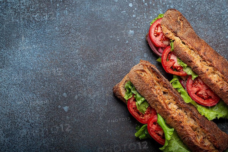 Two dark ciabatta sandwiches with green salad, ripe red tomatoes, onion and tuna on rustic concrete stone background top view. Vegetable vegetarian sandwiches, healthy snack or lunch. Space for text, food photography