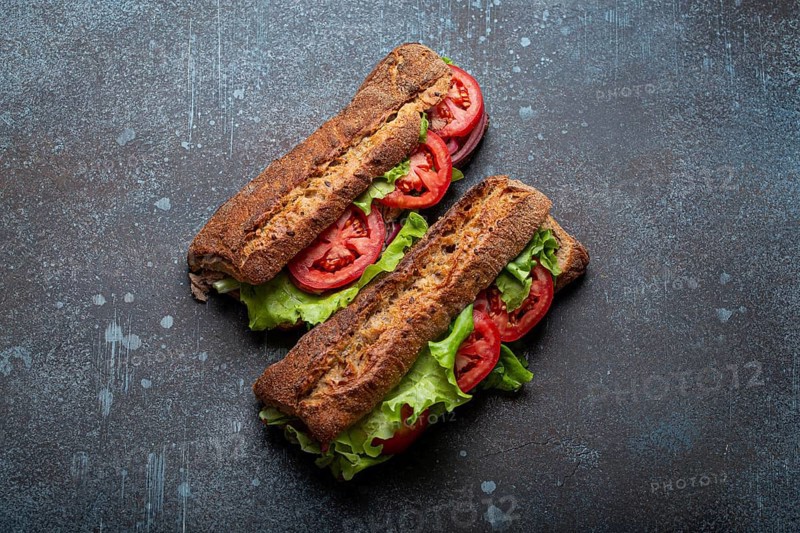 Two dark ciabatta sandwiches with green salad, ripe red tomatoes, onion and tuna on rustic concrete stone background top view. Vegetable vegetarian sandwiches, healthy snack or lunch, food photography, food photography