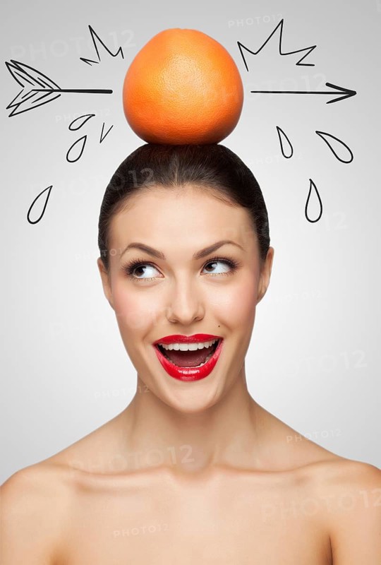 Creative portrait of a beautiful smiling woman holding a red grapefruit pierced with a sketchy arrow on her head