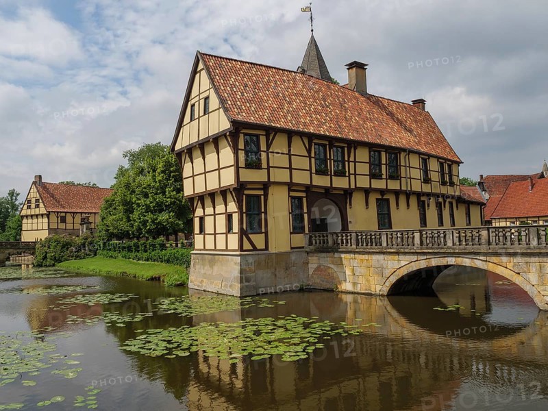 Half-timbered house stands picturesquely on a watercourse with water lilies and a stone bridge, steinfurt, münsterland, germany