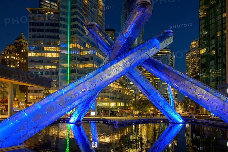 Modern Olympic fire installation at night with blue lighting and surrounding skyscrapers in the city, Vancouver, British Columbia, Canada, North America