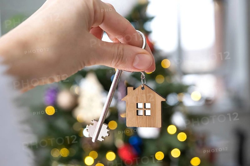Key and tiny house keychain in hand on background fairy lights Christmas tree. gift for New Year, Christmas. Building, design, project, moving, insurance, mortgage, rent and purchase real estate