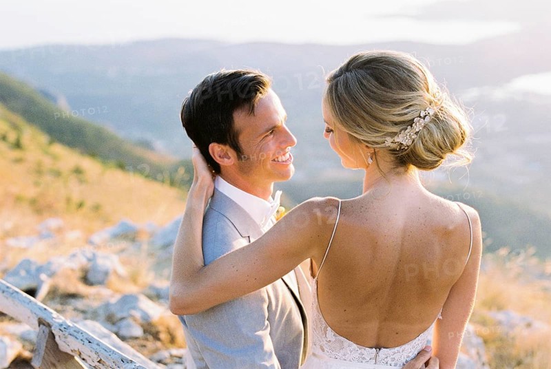 Bride sits on the lap of groom, hugging his shoulders.