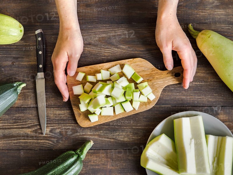 Zucchini harvest. Woman slices zucchini cubes for freezing on wooden table. Farm organic zucchini harvesting Top view or flat lay