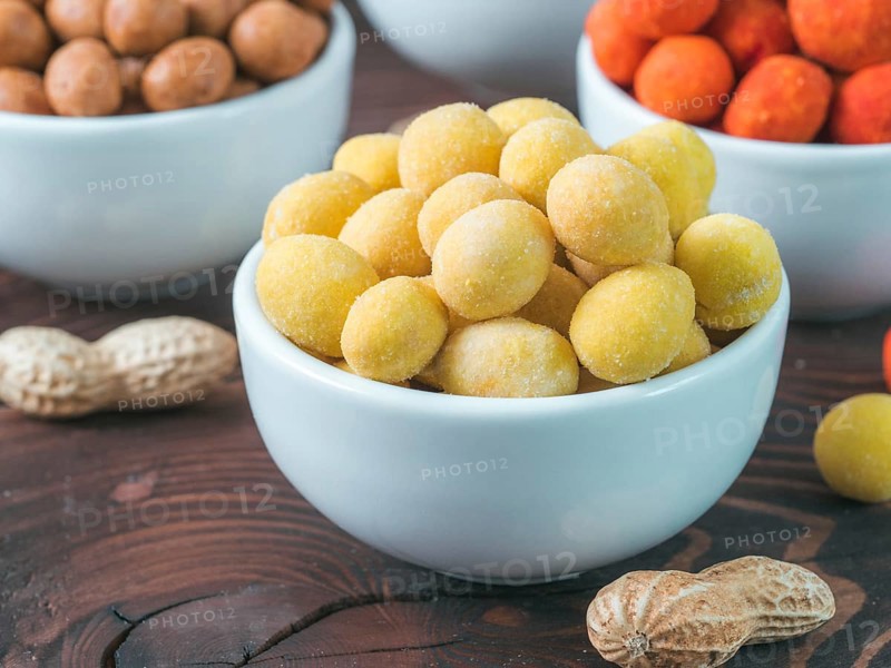 Peanut snack for beer, wine, party bar. Salted peanuts in yellow cheese glaze on brown wooden table. Copy space