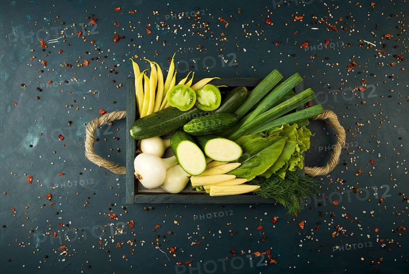 FRESH VEGETABLES ON WOODEN BOX ON A DARK STONE BACKGROUND. THE CONCEPT OF VINTAGE. THE YOUNG CORN ONIONS ASPARAGUS GREEN TOMATO CUCUMBER ON A DARK SURFACE