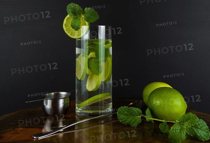 Glass of Mojito cocktail with mint and lime on a black board with fresh limes. Sparkling refreshing water. Place for text