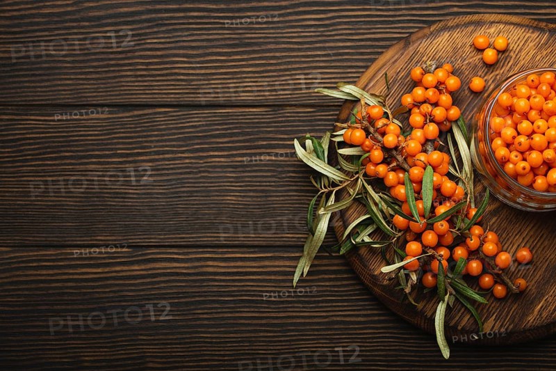 Sea buckthorn ripe berries in glass jar and branches with leaves top view on dark wooden rustic background, great for skin, heart, vessels and immune system. Copy space, food photography, food photography