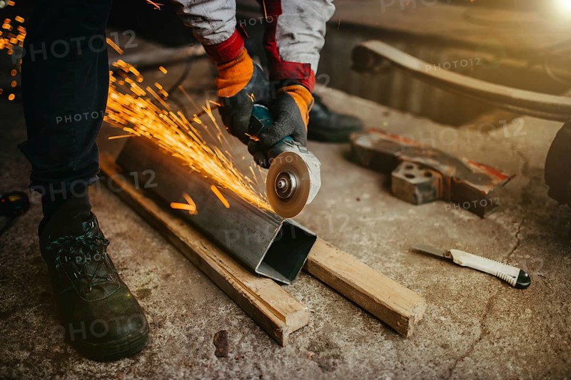 A worker grinding metal with sparks flying, wearing protective gloves