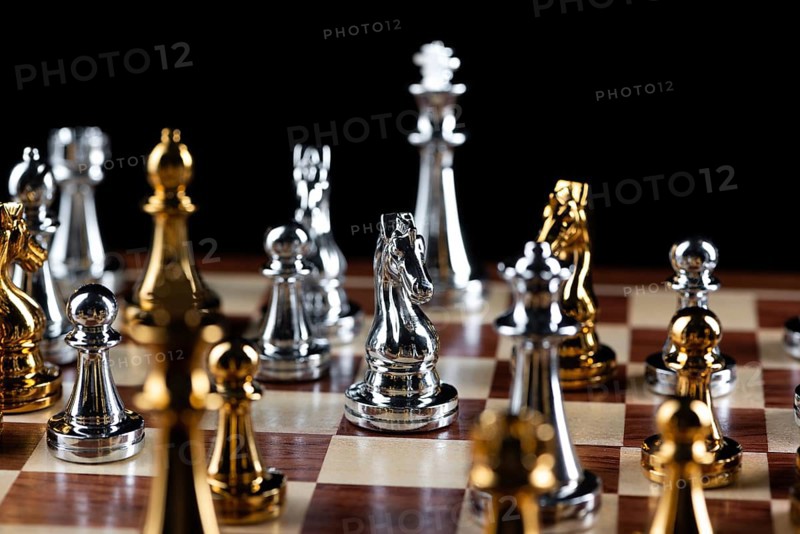 Gold and silver chess figures standing on chessboard. Intellectual and tactic game. Strategy planning, leadership and teamwork business concept. Close-up metal chess pieces on black background
