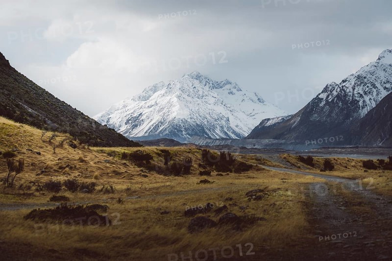 Gravel track leads through a vast landscape with snow-capped mountains and cloudy skies, Hooker Valley Track, New Zealand, Oceania