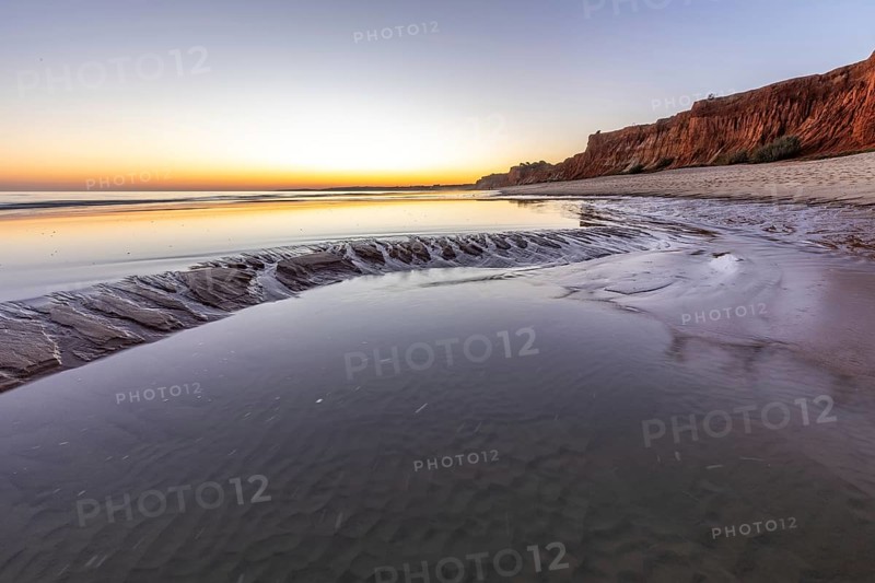Sea with reflection at low tide in the calm waters of the Atlantic. Landscape shot of the sunset on the cliffs and the sandy beach of Praia do Poço Velho, Praia da Falésia, Quarteira, Algarve, Portugal, Europe