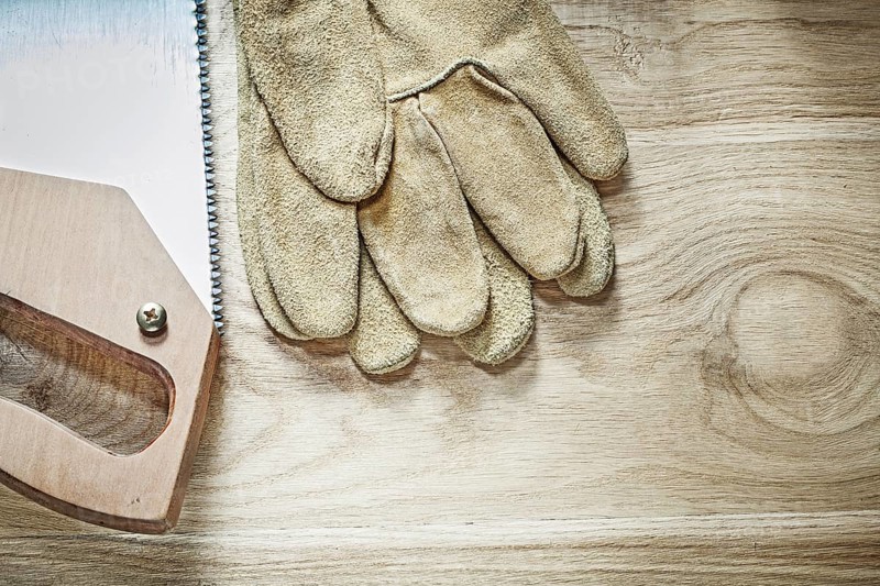 Safety gloves handsaw on wooden board top view construction concept