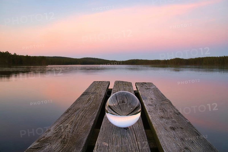 Glass ball on a wooden pier at a Swedish lake at evening hour. Nature shot from Scandinavia