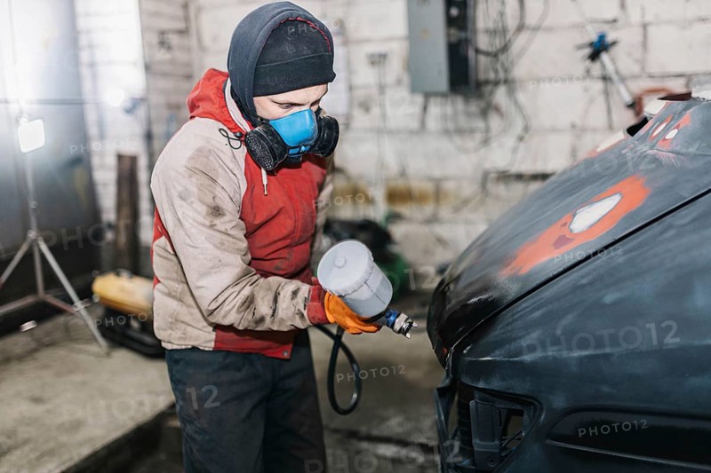 Worker spray painting a car hood in a workshop environment