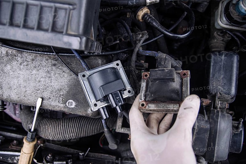 Close-up of a hand holding a car ignition coil in an engine