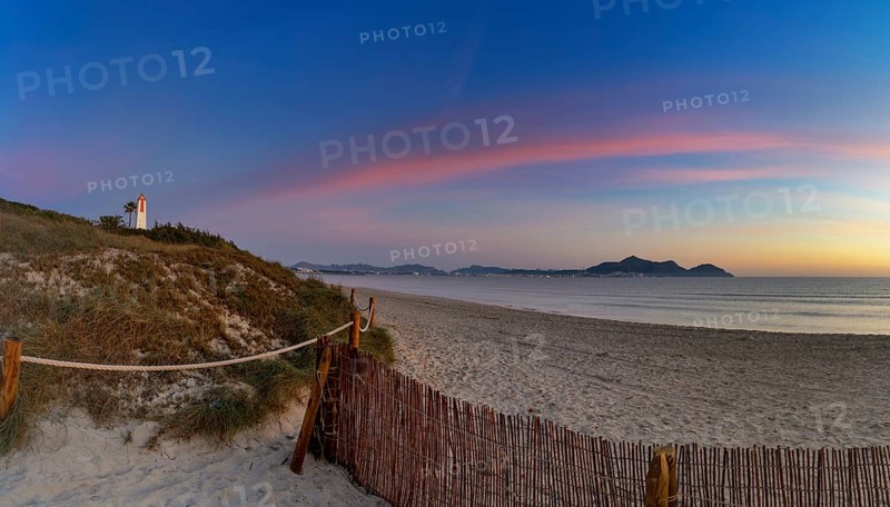 Picturesque Playa del Muro beach with sand dunes and a view of the historic maritime observation towers and the town of Alcudia in the background