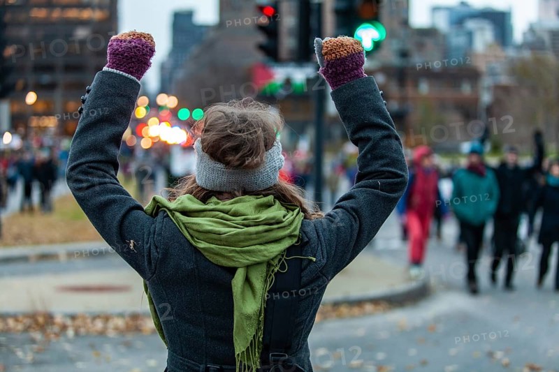Young woman is raising her arms high while looking at the crowd during an ecological protest. Shot from the back