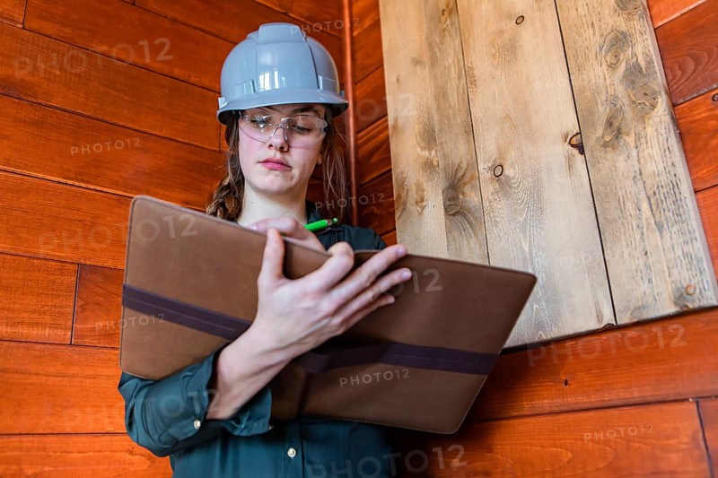 Construction female inspector using a clipboard to taking notes. a young caucasian woman worker wearing hard hat at work, low angle portrait