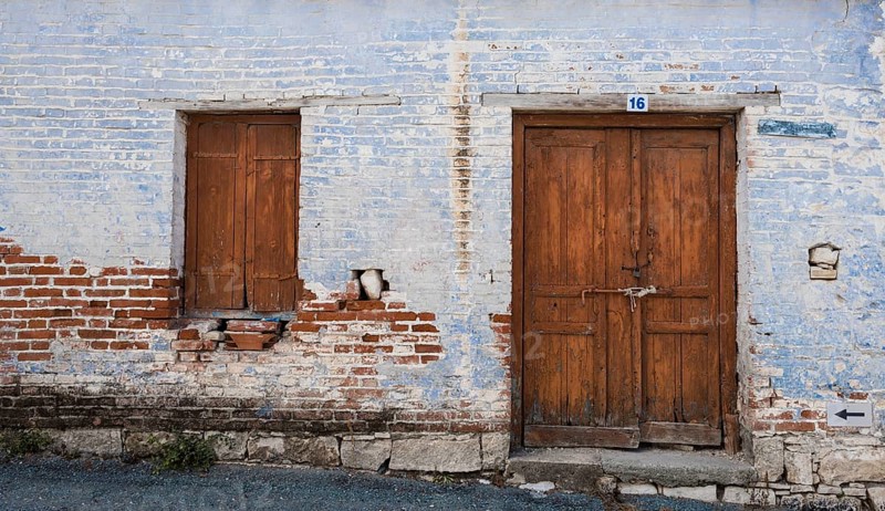 Exterior of an old village house with blue stoned wall and closed vitnage door and window