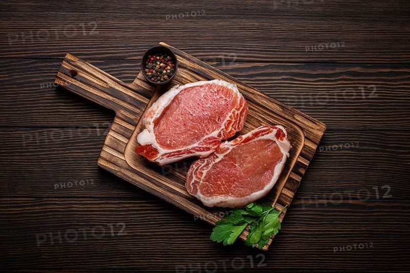 Cut raw meat pork steaks with seasonings on kitchen cutting board, rustic wooden background top view, ready for BBQ. Pork loin chops, food photography, food photography