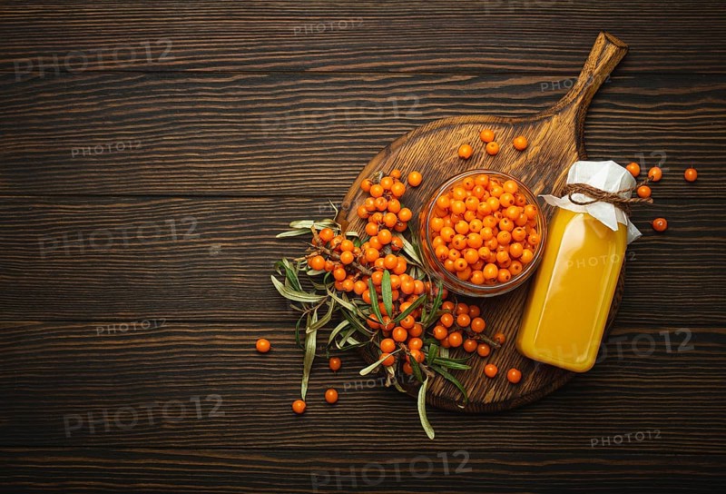 Sea buckthorn healthy drink in bottle, ripe berries in glass jar and branches with leaves top view on dark wooden rustic background, great for skin, heart, vessels and immune system. Copy space, food photography, food photography