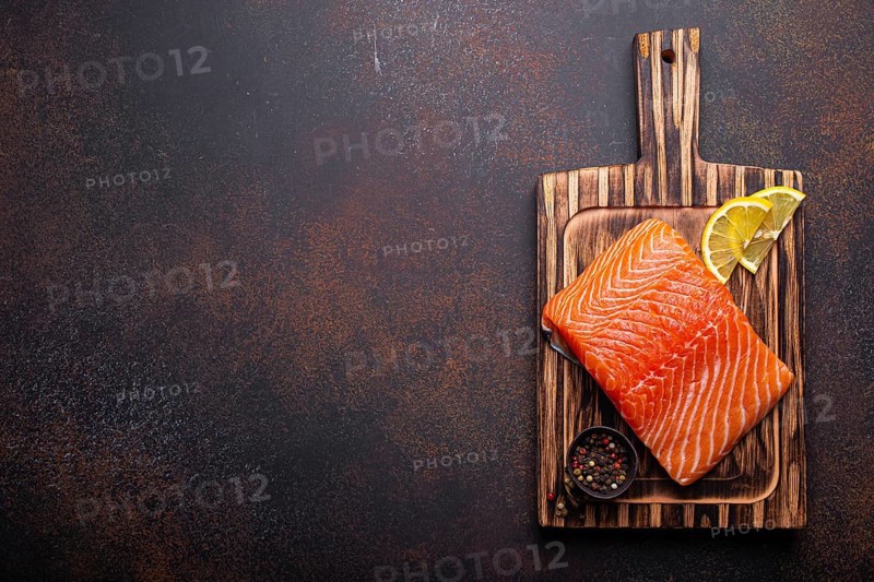 Fresh raw salmon fillet on wooden kitchen cutting board with seasonings and lemon top view on dark brown rustic background, space for text, food photography, food photography