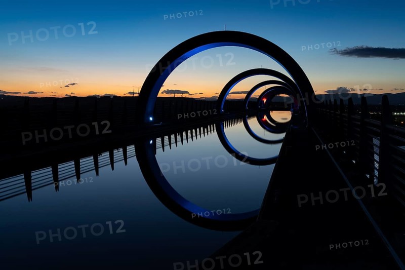 A view of the Falkirk Wheel at sunset with lights in different bright colors