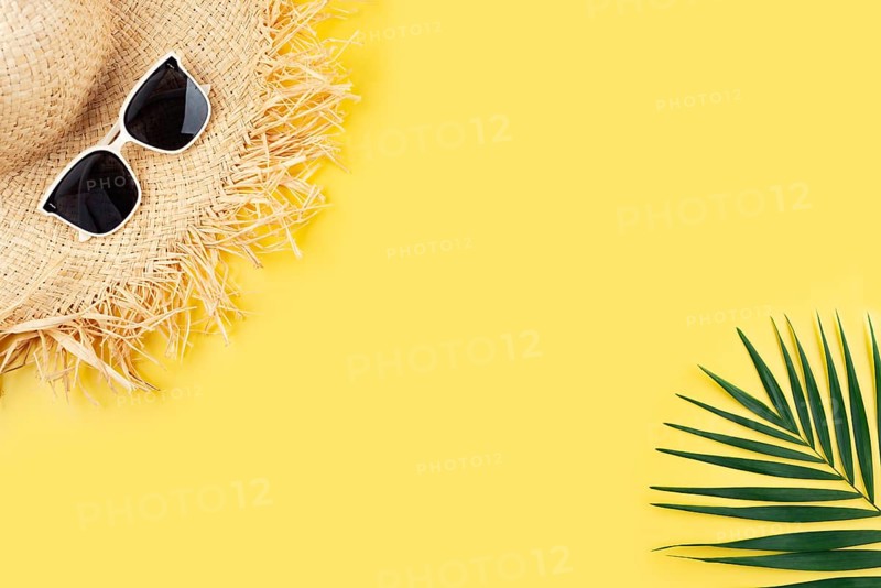 Vacation travel planning simple theme of straw hat sunglasses and palm leaves on uniform yellow background flat lay with copy-space