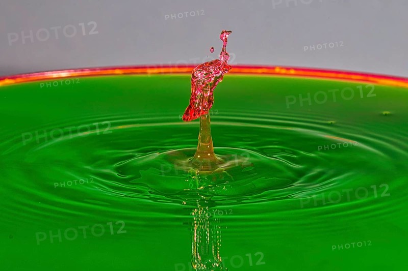 A red water drop rises dynamically on a green background, water drop, collision, high-speed photography, concept, water figures