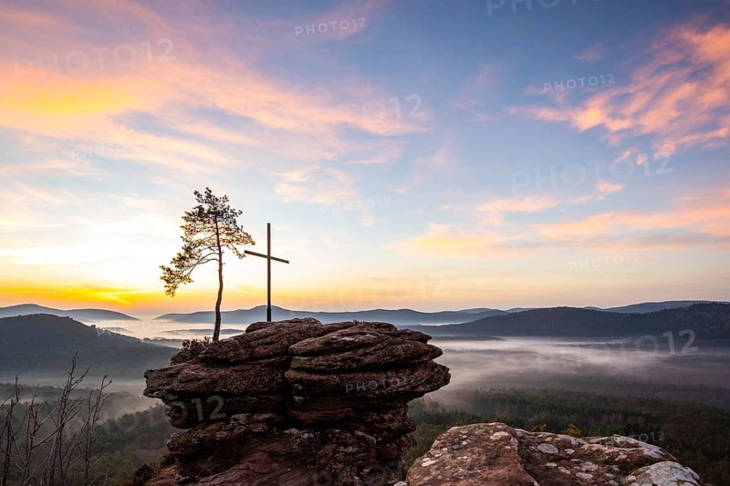 Landscape shot of nature in the morning. Mist in the valley and a summit cross on a sandstone cliff. Sunrise in the Palatinate Forest, Germany, Europe
