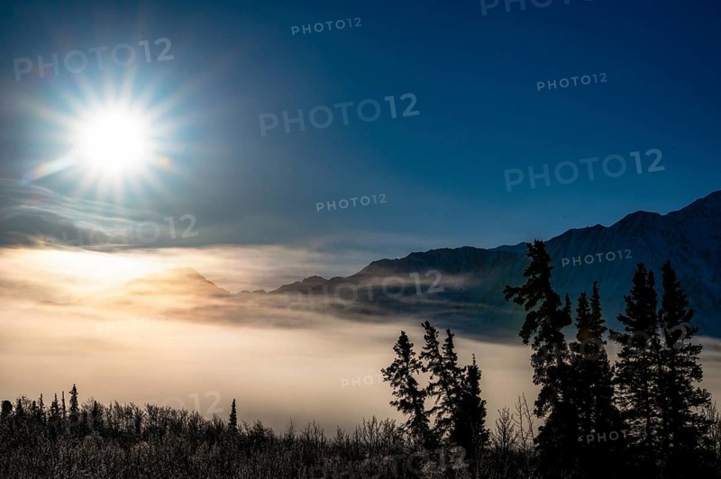 Sun over foggy, snow-covered landscape with mountain silhouette, Yukon, Canada, Kluane National Park, North America