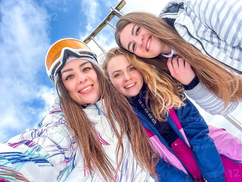 Group of happy friends skier taking selfie hiking mountains. Girls smiling Makes Selfie In Ski Clothing On Snow Mountain. Resting relaxing extreme recreation active lifestyle activity technology smart phone mobility internet online concept. Emotions nature on background