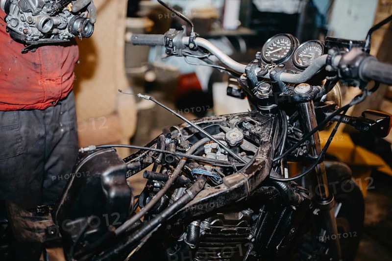 Mechanic repairing motorcycle in a workshop, focusing on engine and gauges