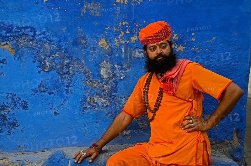 Priest saffron sitting against blue wall, Jodhpur, Rajasthan, India, Asia