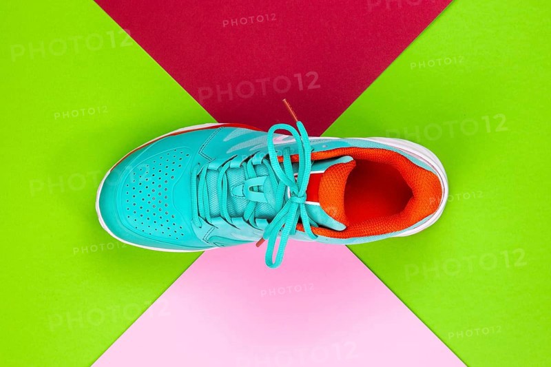 Red, cyan, white new tennis shoe in studio shot over green, pink, purple background. Directly from above