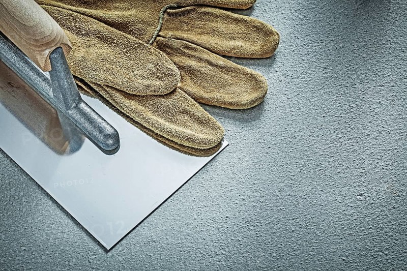 Stainless bricklaying trowel leather protective glove on concrete background construction concept