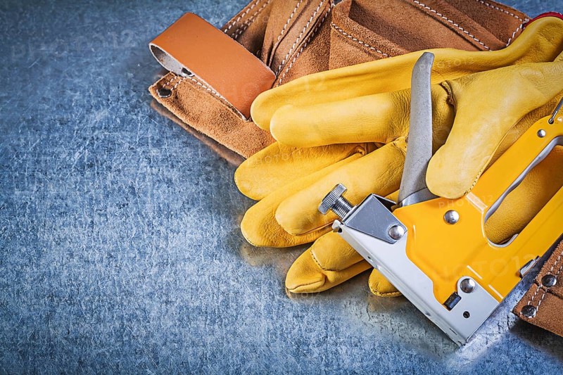 Composition of leather tool belt safety gloves stapler gun on metallic background construction concept